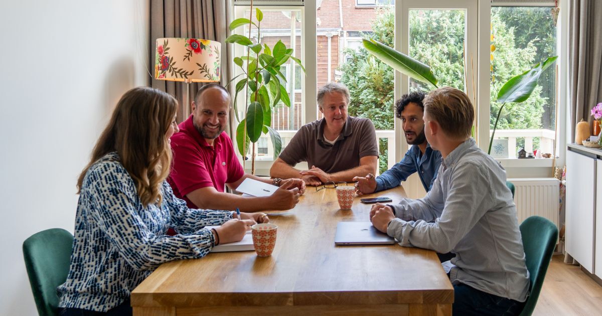 Vijf collega's in overleg rond een tafel met laptop en aantekeningen